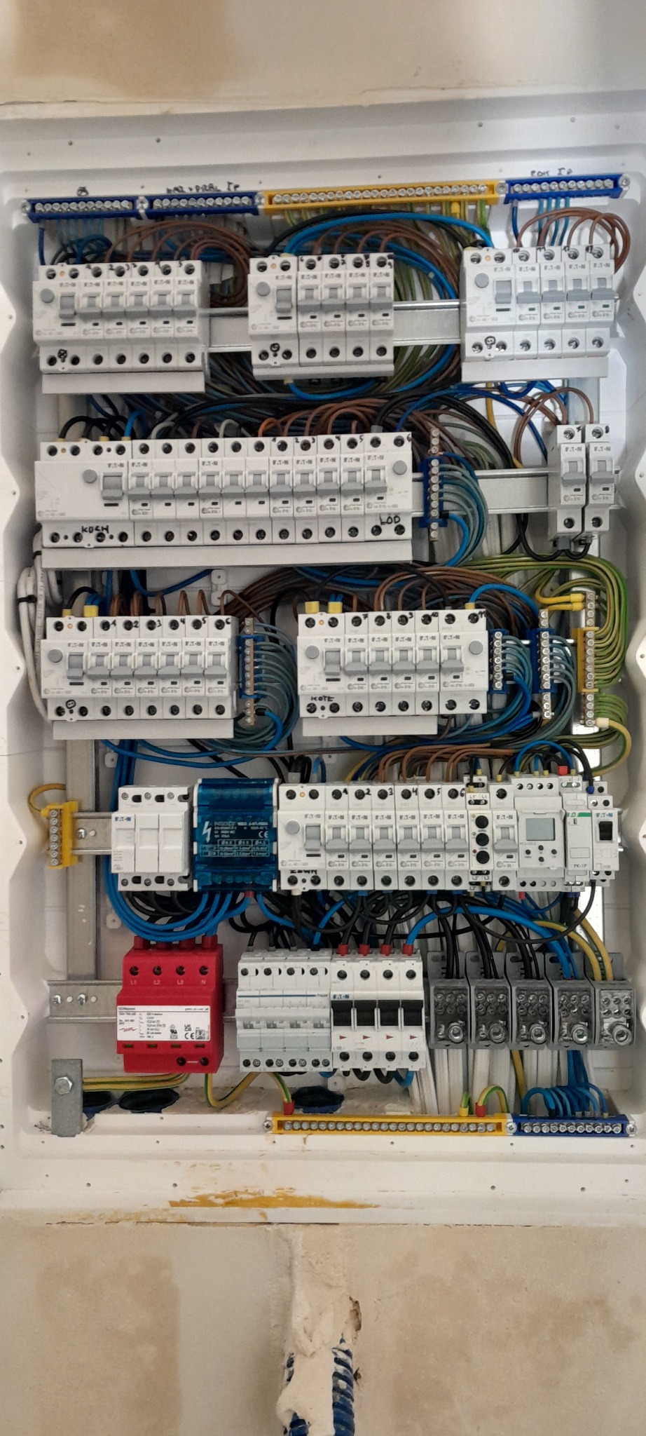 Rozdzielnica elektryczna z zabezpieczeniami różnicowoprądowymi i nadprądowymi, okablowana wewnątrz białej obudowy. Widoczne przewody w różnych kolorach i listwy zaciskowe.