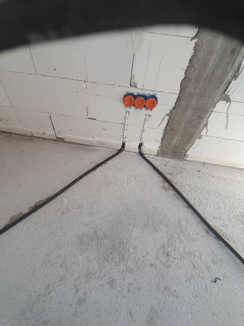 Instalacja elektryczna w surowym stanie: trzy pomarańczowe puszki podtynkowe zamontowane w białej ścianie z betonu komórkowego, z wyprowadzonymi przewodami w peszlach.