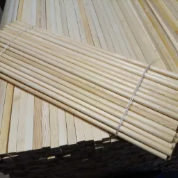 Stos okrągłych, jasnych listew drewnianych związanych sznurkiem, ułożonych na stosie tarcicy budowlanej.