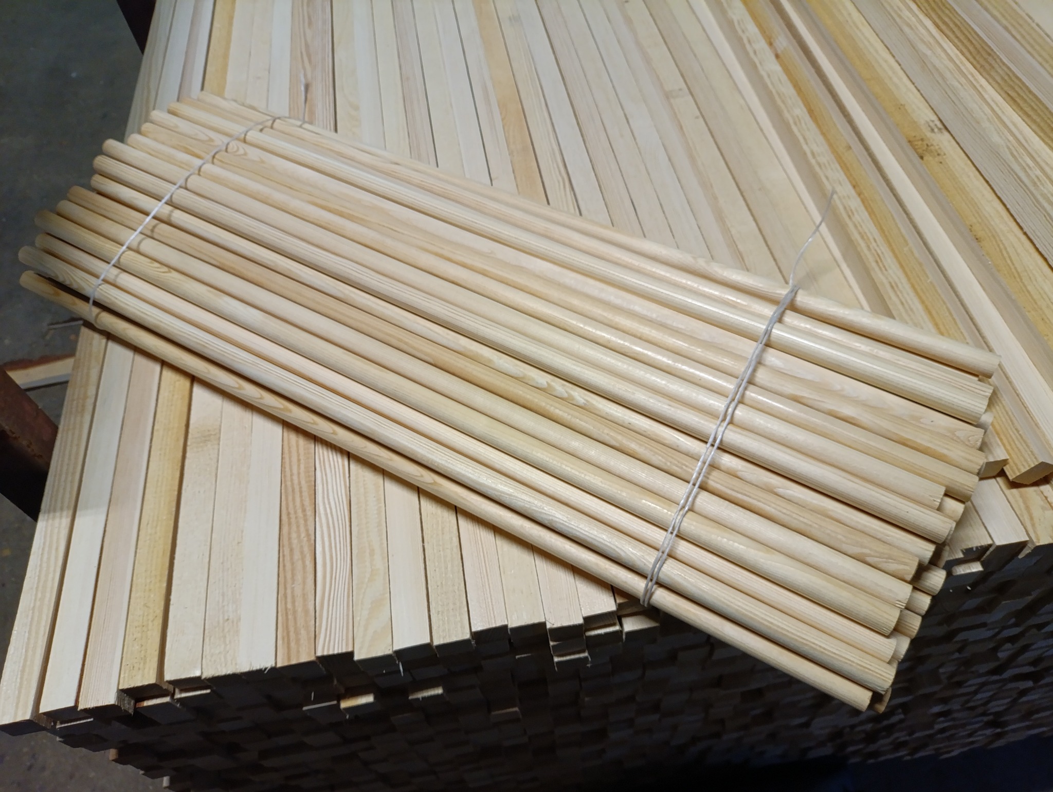 Stos okrągłych, jasnych listew drewnianych związanych sznurkiem, ułożonych na stosie tarcicy budowlanej.