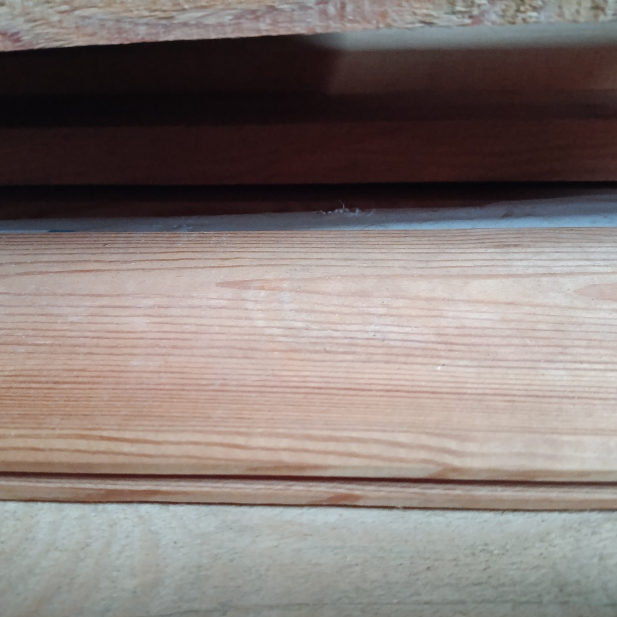 Fragment ułożonych desek z widocznymi słojami drewna i niewielkimi zabrudzeniami, ujęcie z bliska.