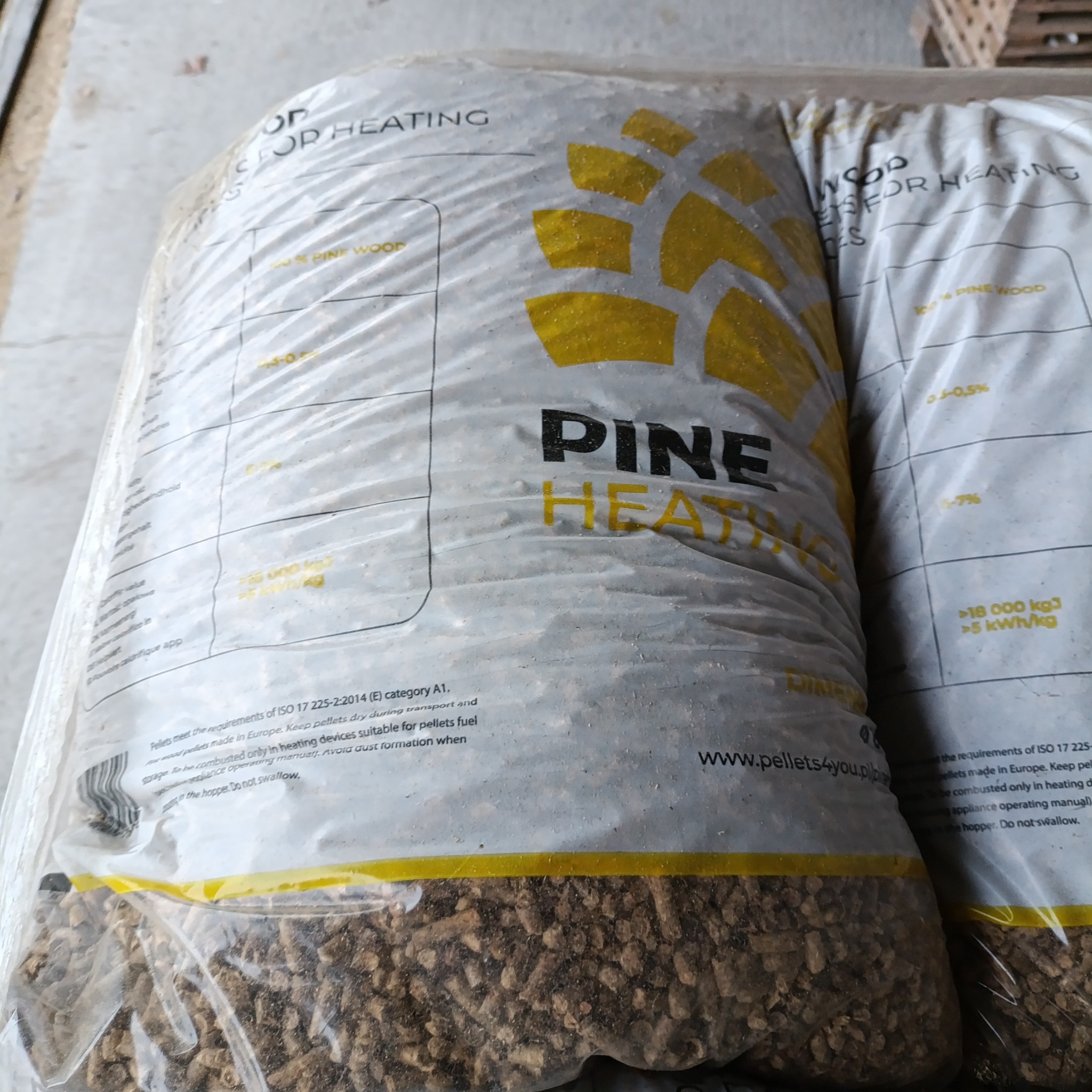 Dwa worki z przezroczystego tworzywa wypełnione brązowymi, drobnymi granulkami, etykieta z napisem 'PINE HEATING'.