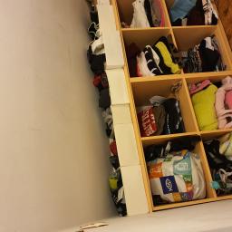 Sevis-An - Wnętrze szafy z półkami wypełnionymi ubraniami, tekstyliami i torbą na zakupy z kolorowymi wzorami, widok z dołu.