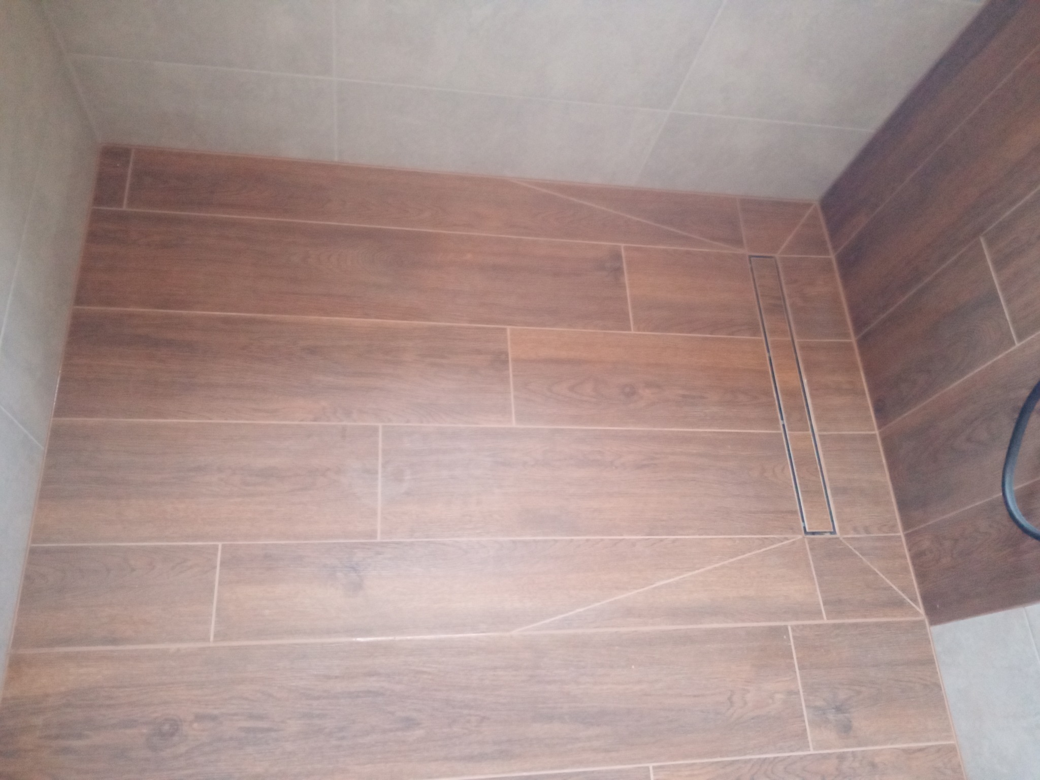 Wykończona kabina prysznicowa z drewnopodobnymi płytkami i liniowym odpływem, widok z góry.