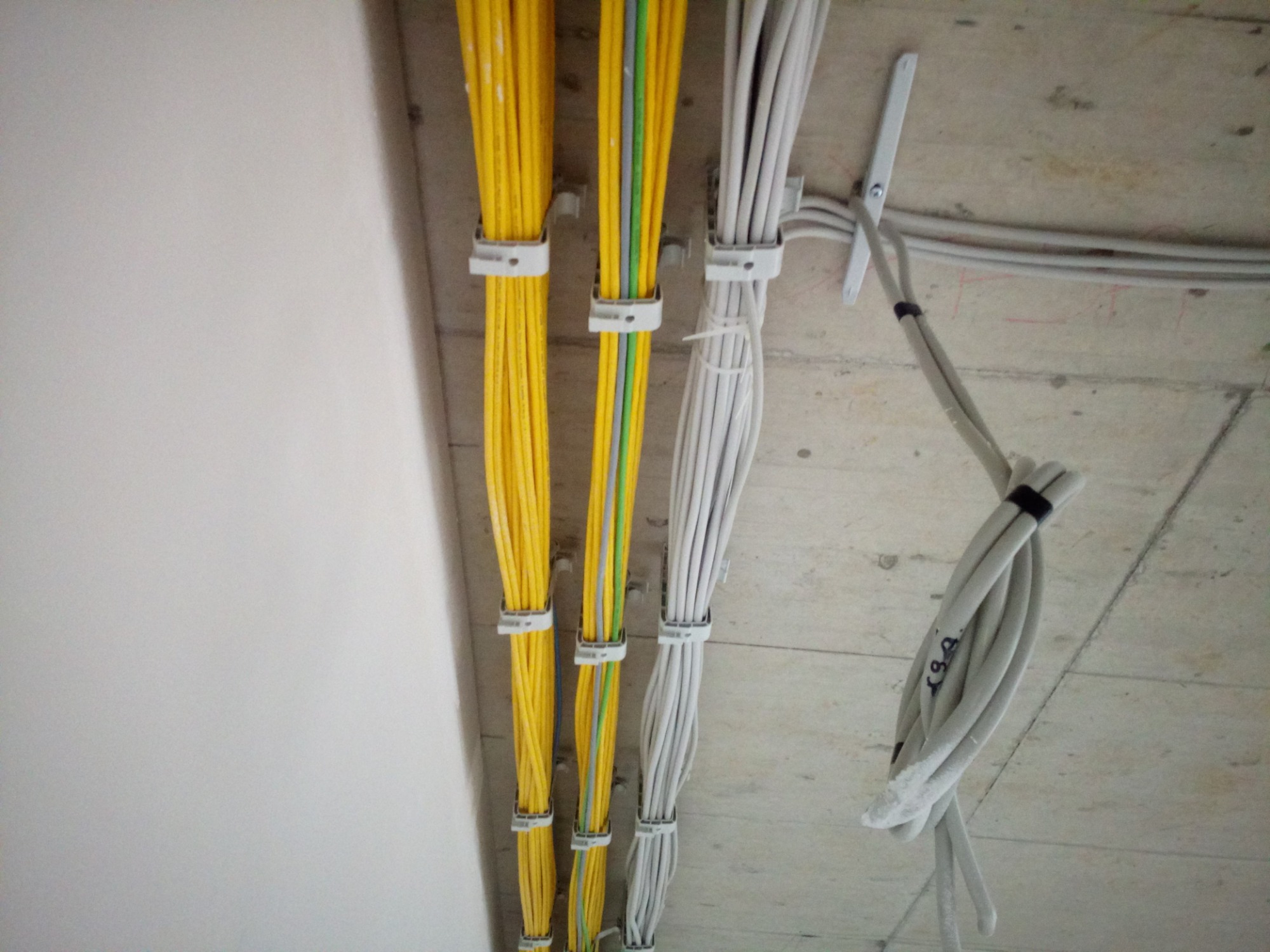 Wiązki przewodów elektrycznych w kolorach żółtym, szarym i białym, przymocowane do sufitu za pomocą plastikowych uchwytów. Jeden przewód szary jest dodatkowo spięty czarną opaską.