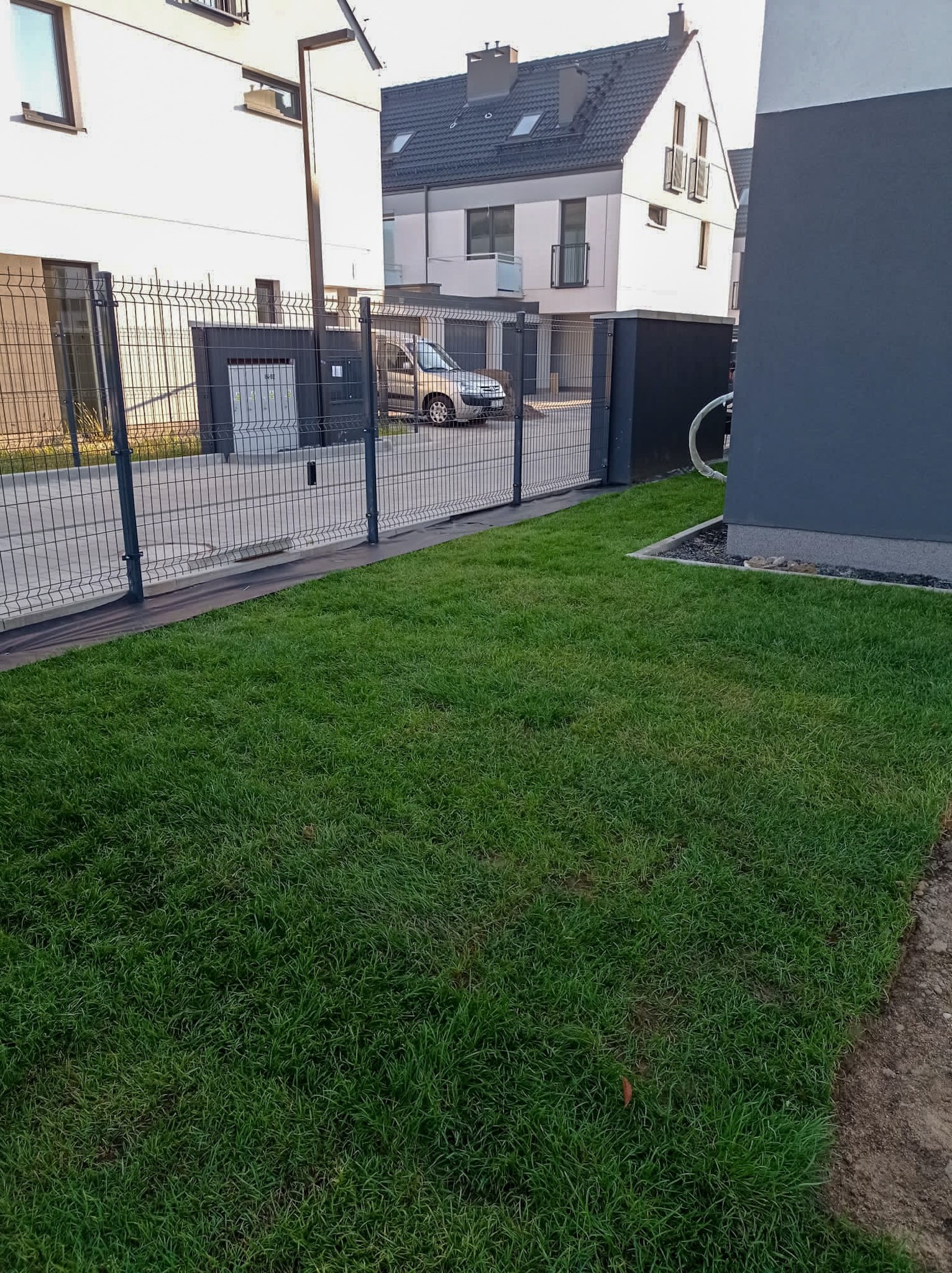 Świeżo założony trawnik z rolki przy nowoczesnym domu jednorodzinnym we Wrocławiu, widoczna siatka ogrodzeniowa i fragment elewacji budynku.