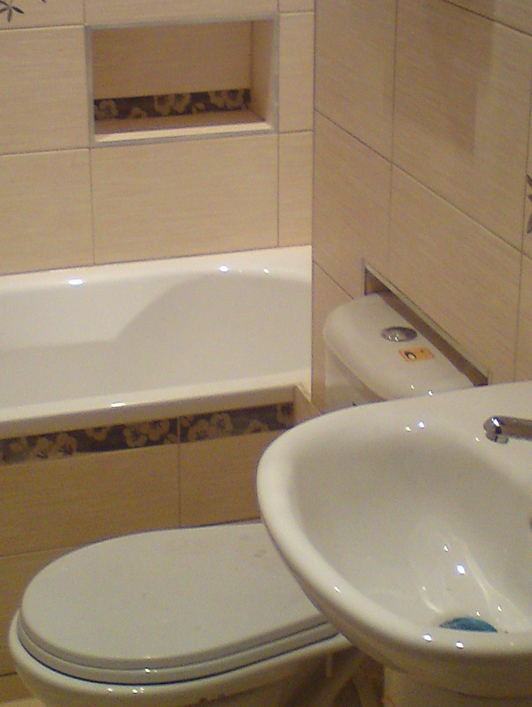 Jasna łazienka w Poznaniu po remoncie: wanna, umywalka i toaleta z beżowymi płytkami i dekoracyjnym pasem nad wanną.