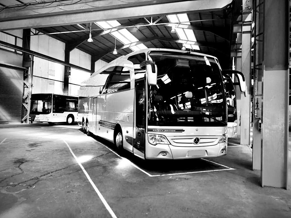 Dwa autobusy Mercedes-Benz zaparkowane w hali garażowej z betonową podłogą i oświetleniem sufitowym, widoczne słupy konstrukcyjne i oznaczone miejsca parkingowe.