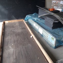 M&S usługi wykończeniowo/budowlane - Przygotowane materiały do ocieplenia: płyty styropianowe w stosie, profile w folii, puste drewniane ramy, czarna płyta imitująca marmur w tle.