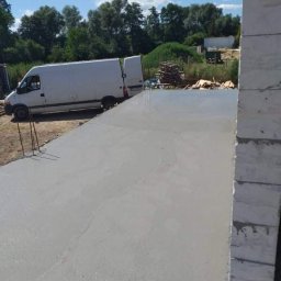 M&S usługi wykończeniowo/budowlane - Świeżo wylana, gładka posadzka betonowa na zewnątrz budynku we Wrocławiu, z widocznym samochodem dostawczym w tle i stosem desek.