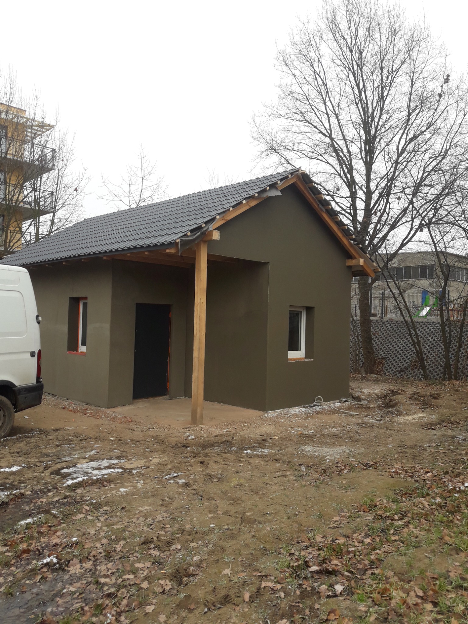 Budynek po nałożeniu surowej, ciemnej elewacji we Wrocławiu, widoczny fragment białego busa i teren z resztkami śniegu.