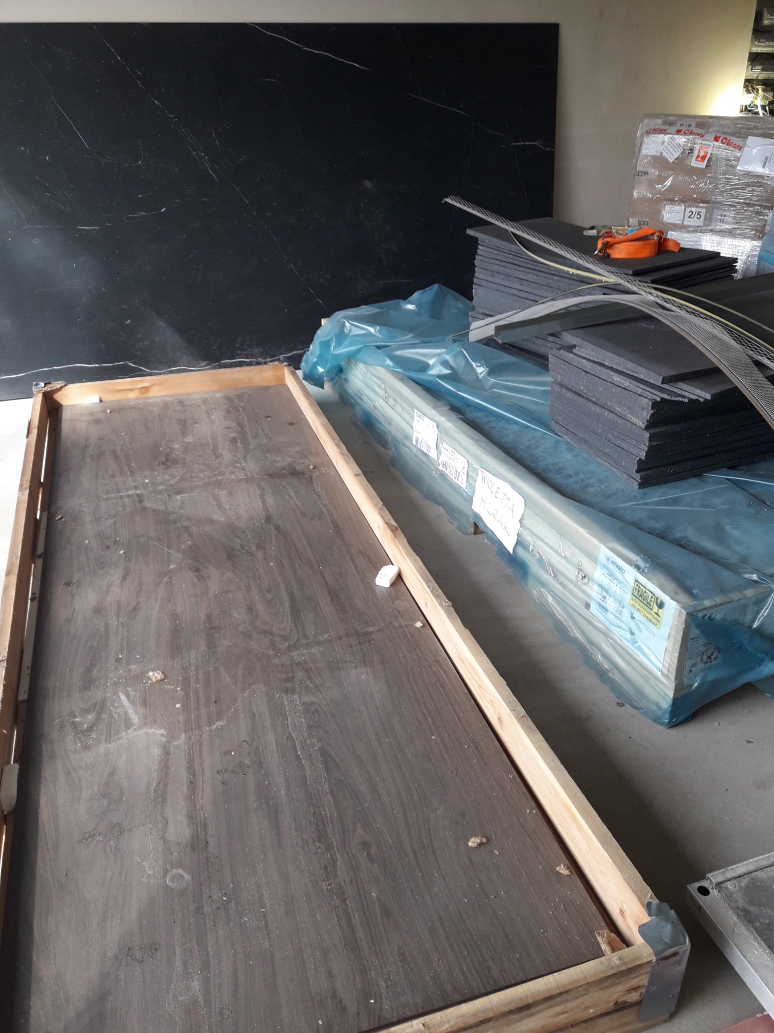 Przygotowane materiały do ocieplenia: płyty styropianowe w stosie, profile w folii, puste drewniane ramy, czarna płyta imitująca marmur w tle.