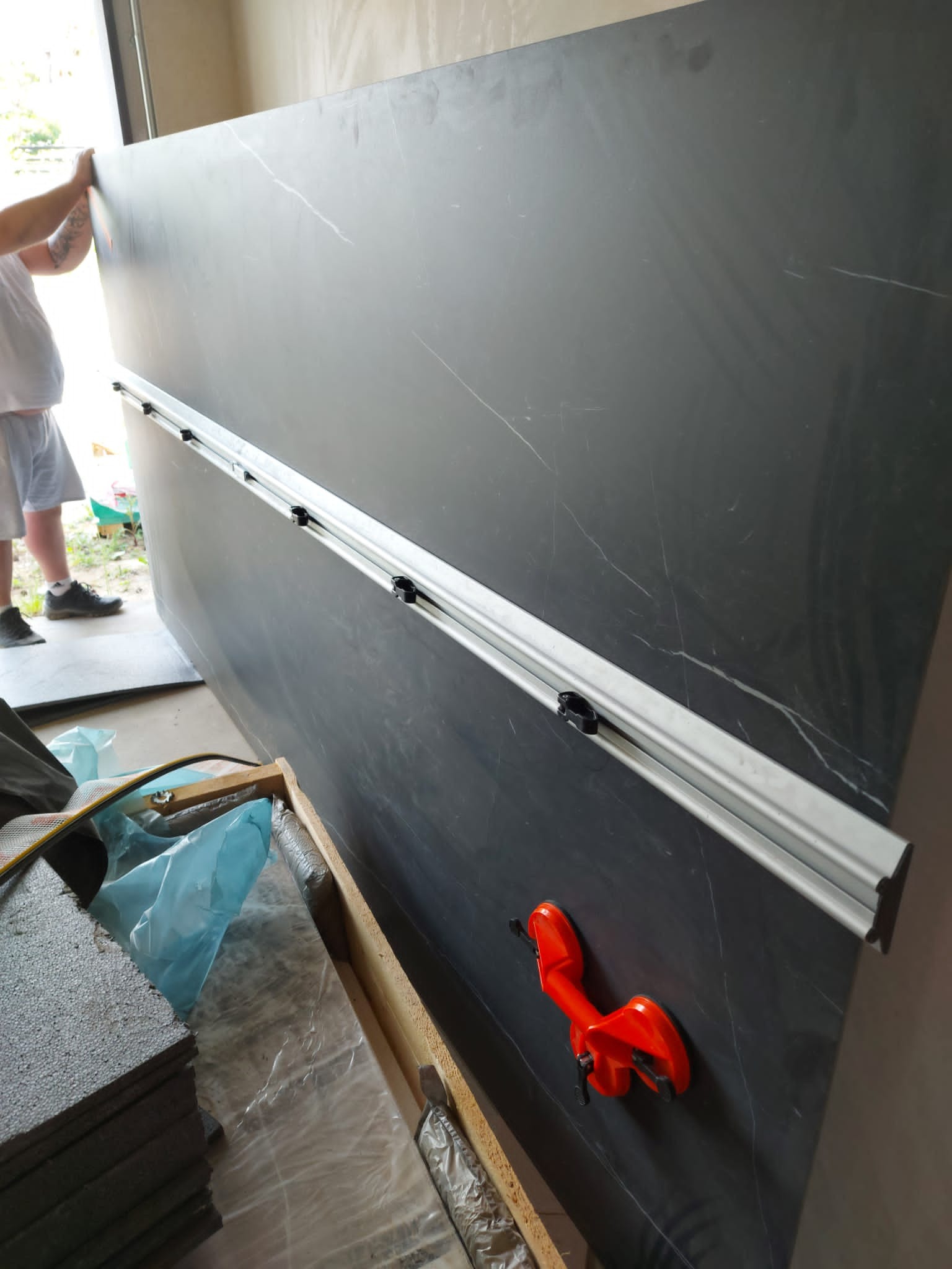 Duża płyta z szarego marmuru z widocznym narzędziem do przenoszenia i listwą prowadzącą, przygotowywana do montażu.