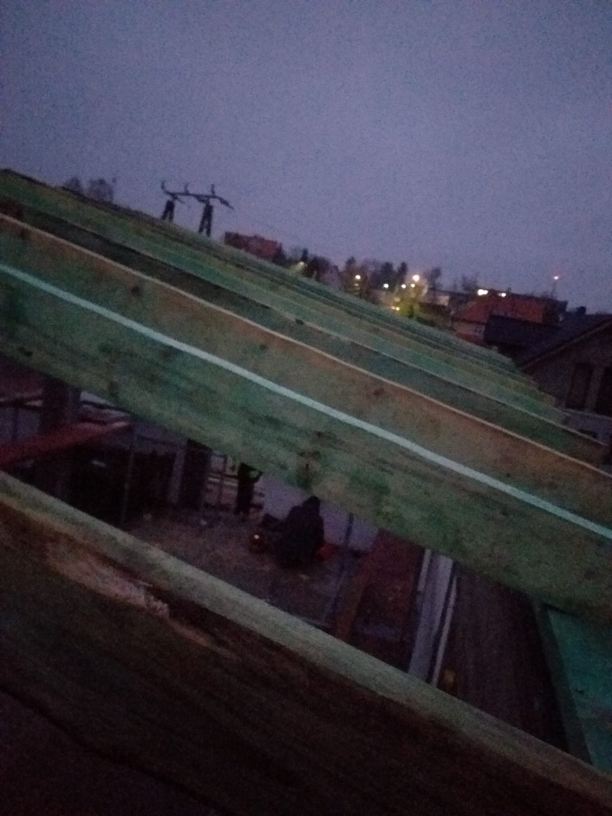 Konstrukcja dachu z drewnianych belek w trakcie budowy, widoczna z perspektywy od dołu w pochmurny dzień, w tle zabudowa jednorodzinna.