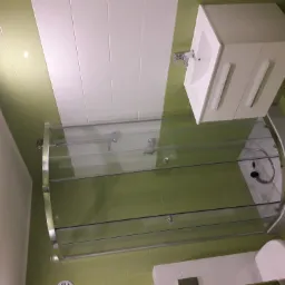 Nowoczesna łazienka z kabiną prysznicową z zaokrąglonymi drzwiami, białą umywalką z szafką i toaletą, wykończona zielono-białymi płytkami.