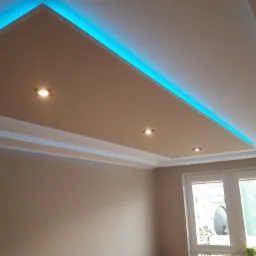 Podwieszany sufit z niebieskim oświetleniem LED i trzema punktowymi lampami, widok na beżowe ściany i okno z widokiem na budynek.