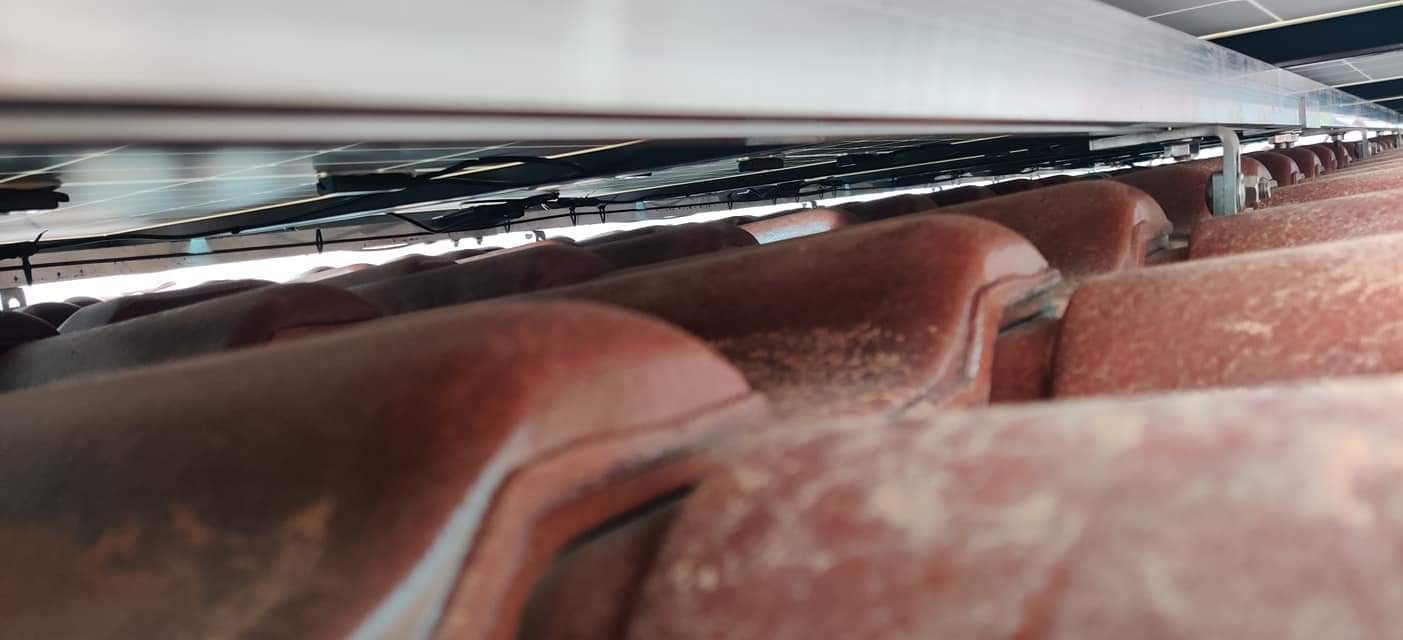 Widok od dołu na panele słoneczne zamontowane na dachu z czerwonej dachówki, widoczne kable i metalowe elementy konstrukcyjne.