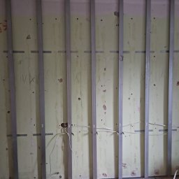 Marcin Owczarek - roboty ogólnobudowlane - Montaż metalowej konstrukcji pod płytę kartonowo-gipsową na starej, częściowo odrapanej ścianie z widocznymi przewodami elektrycznymi.