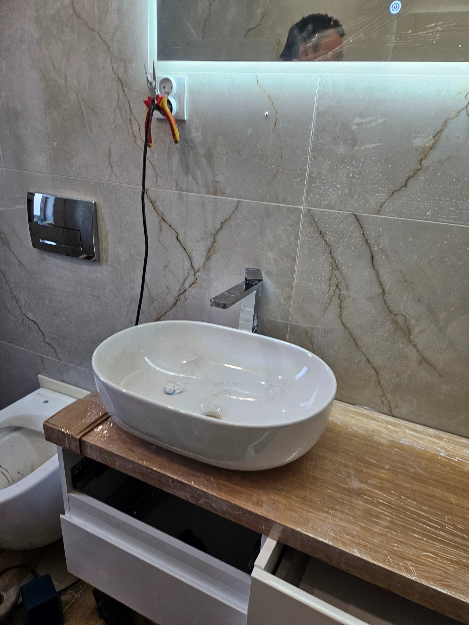 Montaż umywalki nablatowej w łazience z marmurowymi płytkami, blat zabezpieczony folią, widoczne narzędzia elektryczne.