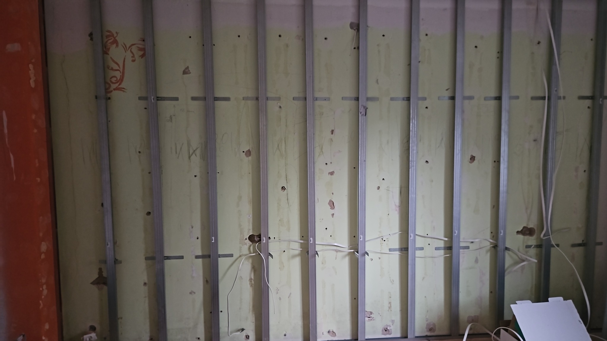 Montaż metalowej konstrukcji pod płytę kartonowo-gipsową na starej, częściowo odrapanej ścianie z widocznymi przewodami elektrycznymi.