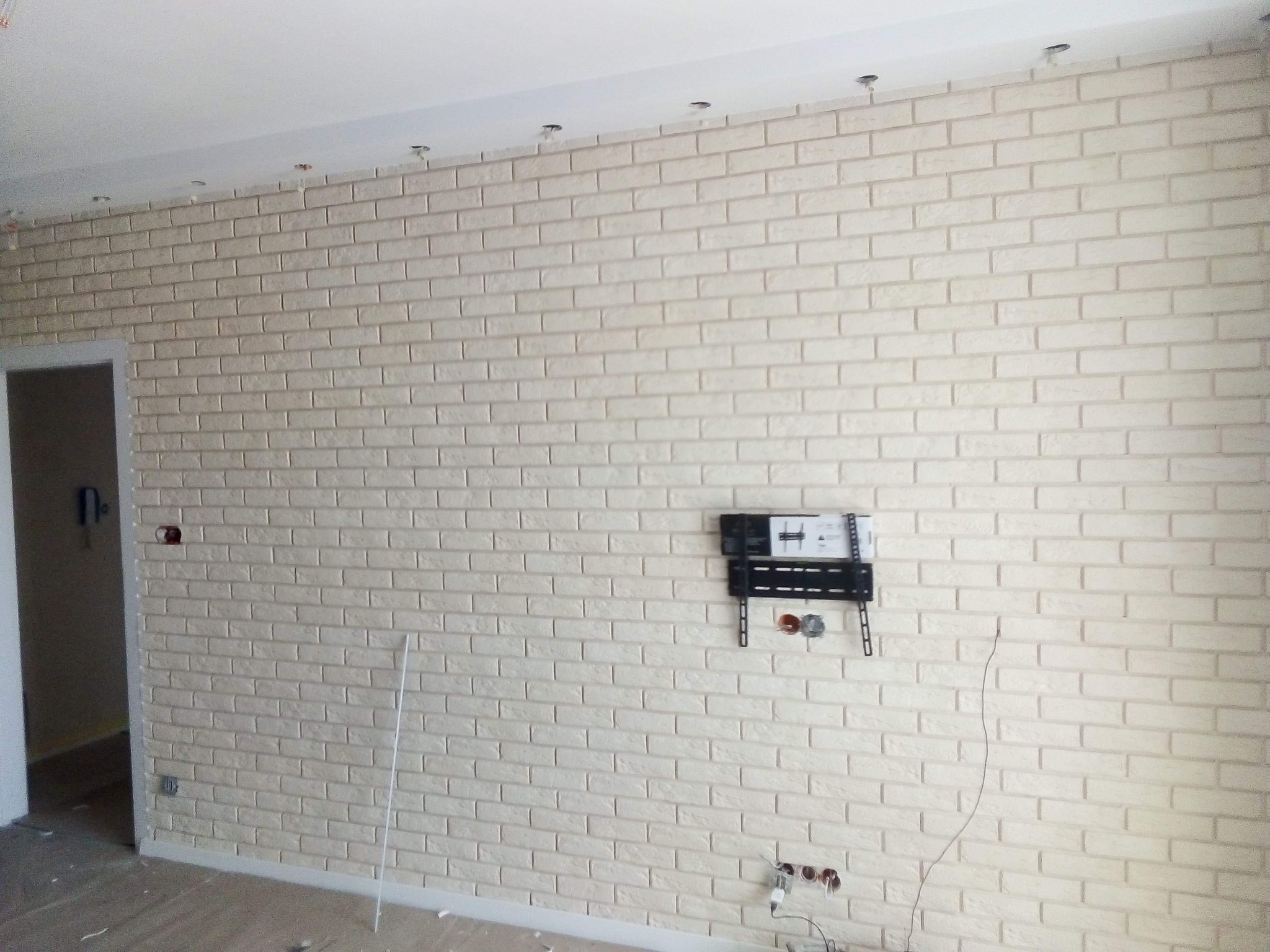 Ściana wykończona dekoracyjną cegłą w Lubawie, z widocznym uchwytem na telewizor i przygotowanymi punktami elektrycznymi, w trakcie prac wykończeniowych.