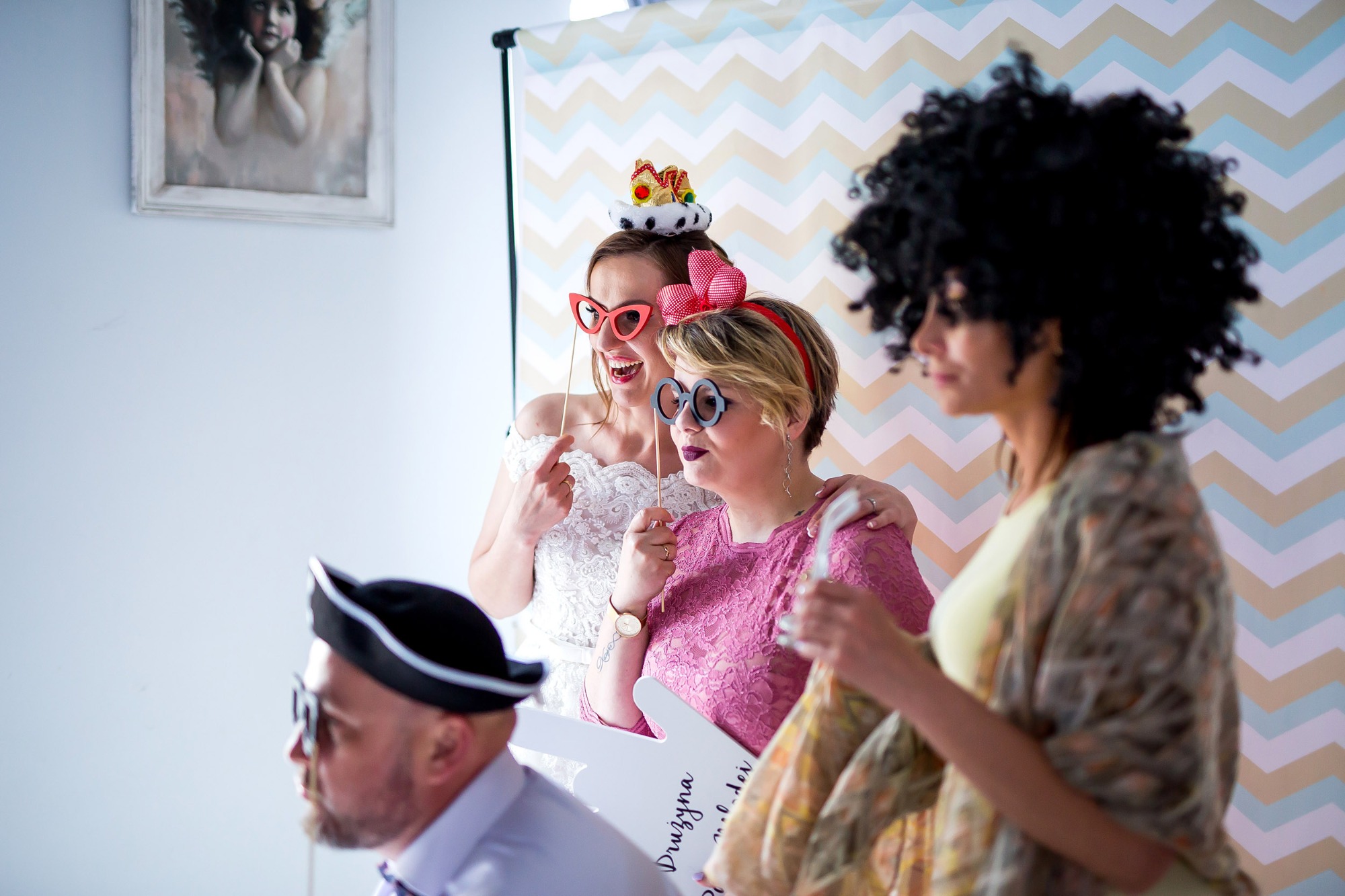 Uczestnicy imprezy w przebraniach i śmiesznych okularach pozują na tle dekoracji w zygzaki, trzymając rekwizyty do zdjęć.