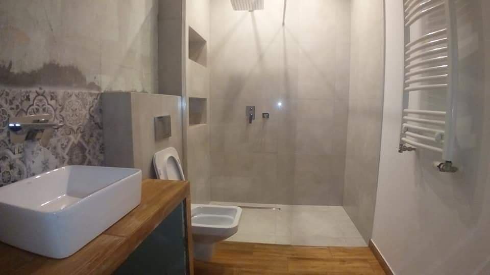 Nowoczesna łazienka z kabiną prysznicową typu walk-in, umywalką nablatową na drewnianym blacie, częściowo wykończona dekoracyjną mozaiką i grzejnikiem drabinkowym.