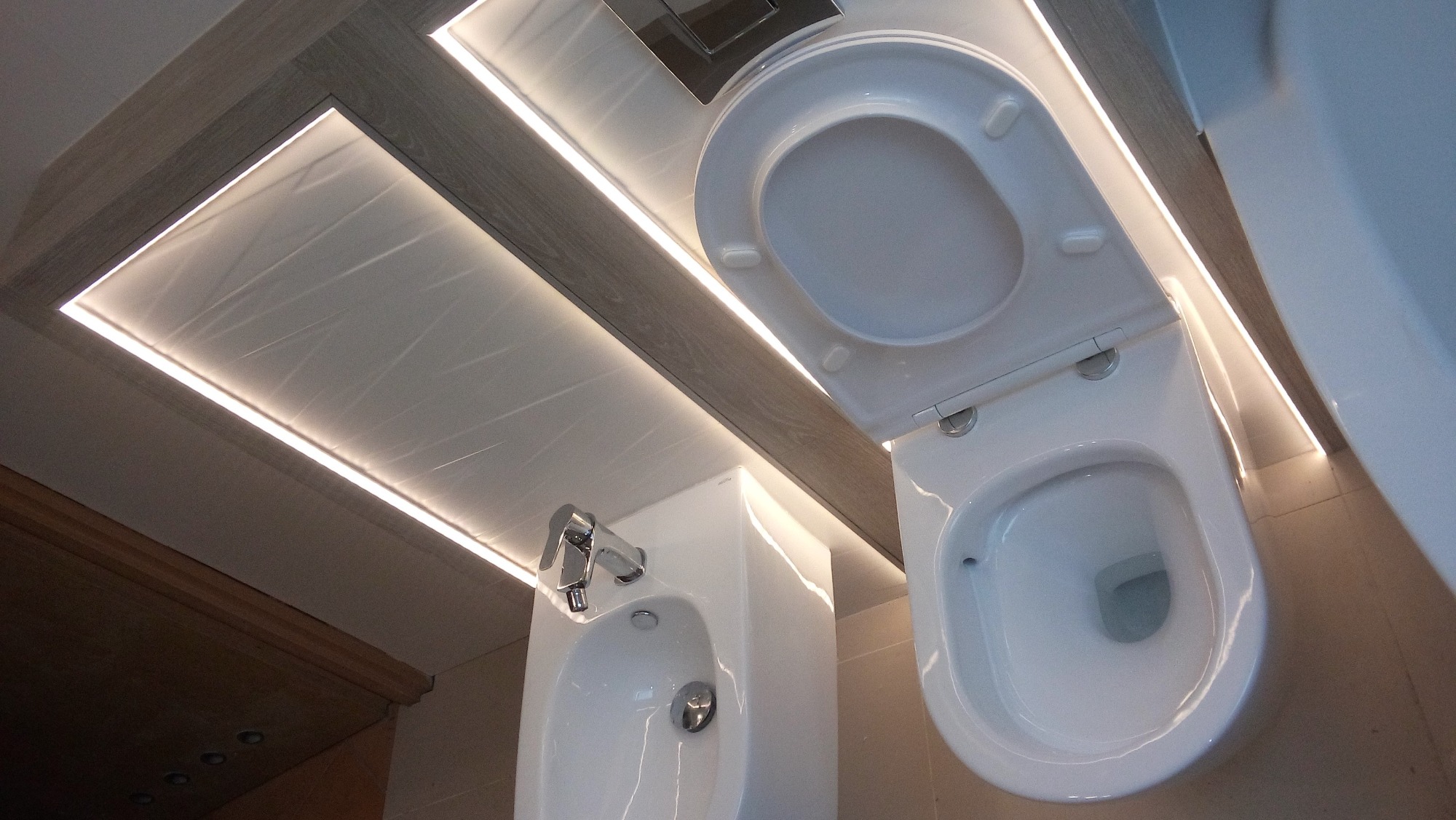 Bidet i toaleta w nowoczesnej łazience z podświetlanym sufitem, widok z dołu.