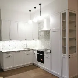 Jasna kuchnia z białymi szafkami, wzorzystą mozaiką nad blatem i trzema wiszącymi lampami kulami nad zlewem, widziana z niskiego kąta.