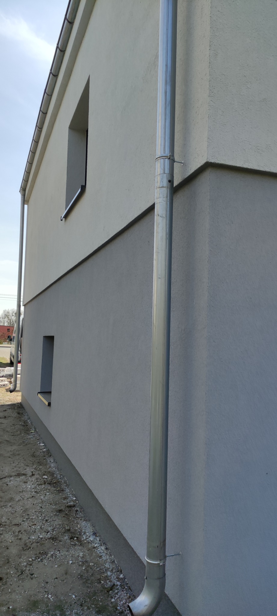 Dwukolorowa elewacja budynku z zamontowaną rynną spustową, widok z boku.