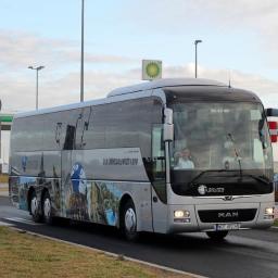 Biuro Podróży Alex - Srebrny autokar MAN z panoramą miast i logo firmy D.A. Kryszalowicz i Syn, stojący na tle stacji benzynowej BP.