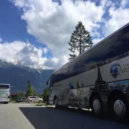 Biuro Podróży Alex - Autokar Biura Podróży Alextour z grafiką wieży Eiffla na tle górskiego krajobrazu i błękitnego nieba z chmurami.
