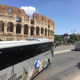 Biuro Podróży Alex - Autokar turystyczny z motywami zabytków świata na tle Koloseum w Rzymie, słoneczny dzień.