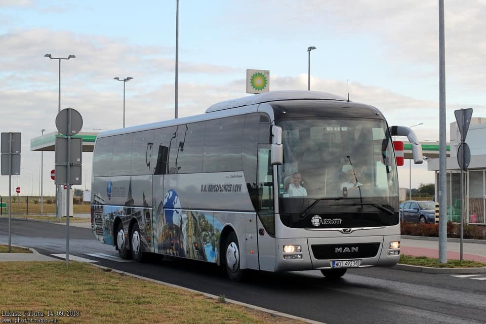 Srebrny autokar MAN z panoramą miast i logo firmy D.A. Kryszalowicz i Syn, stojący na tle stacji benzynowej BP.