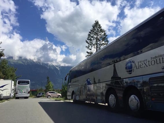 Autokar Biura Podróży Alextour z grafiką wieży Eiffla na tle górskiego krajobrazu i błękitnego nieba z chmurami.