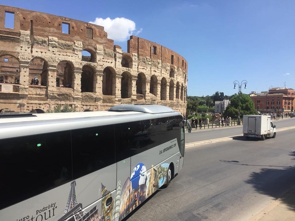 Autokar turystyczny z motywami zabytków świata na tle Koloseum w Rzymie, słoneczny dzień.
