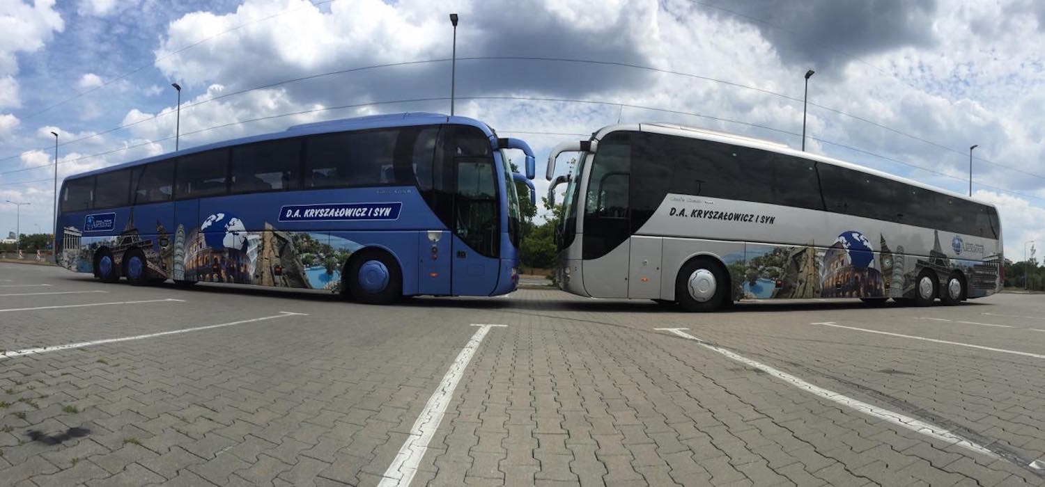 Dwa autokary, niebieski i srebrny, zaparkowane obok siebie na parkingu z namalowanymi atrakcjami turystycznymi na bokach, nazwa firmy D.A. Kryszalowicz i Syn.