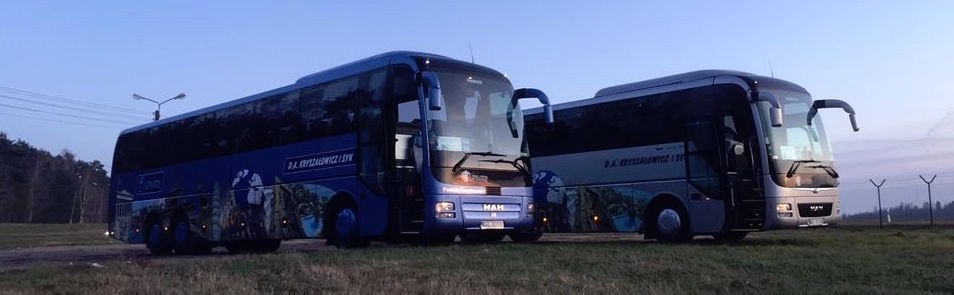 Dwa autokary firmy D.A. Kryształowicz i Syn, jeden niebieski, drugi srebrny, zaparkowane na trawiastym terenie przy zmierzchu.