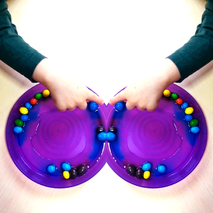 Dziecko układa kolorowe cukierki na fioletowym talerzu, tworząc wzór, widok z góry.