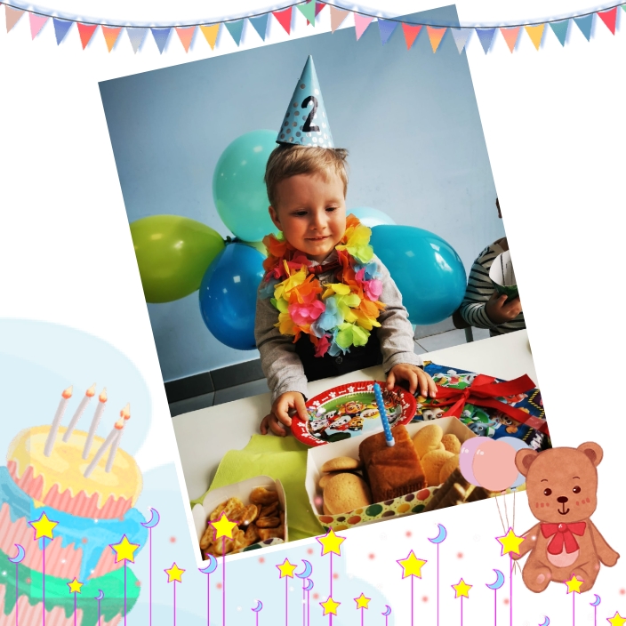 Chłopiec w czapce urodzinowej z numerem 2, w hawajskim naszyjniku, stoi przy stole z przekąskami i balonami, świętując drugie urodziny.