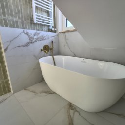 Slawko-bud - Nowoczesna łazienka na poddaszu z wolnostojącą białą wanną, złotą armaturą i marmurowymi płytkami. Uwagę przykuwają pionowe, oliwkowe płytki na ścianie.