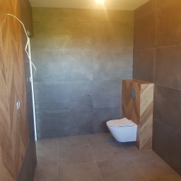 Slawko-bud - Nowoczesna łazienka z szarymi płytkami i drewnianą obudową toalety podtynkowej. Uwagę zwraca wzór jodełki na obudowie i minimalistyczna armatura.