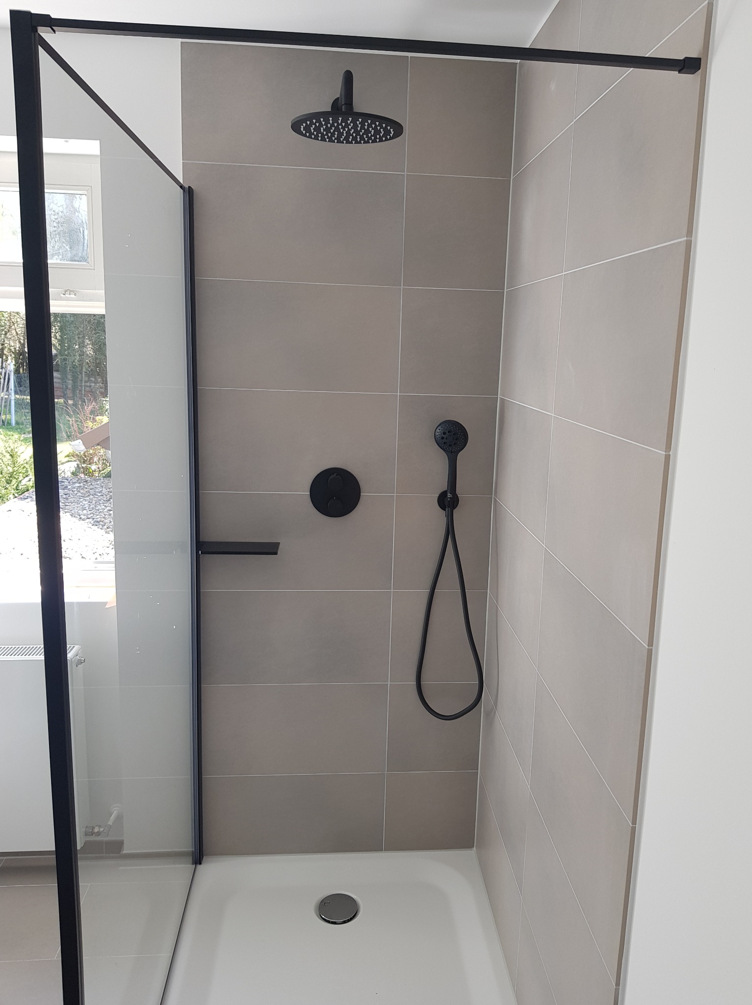 Nowoczesna kabina prysznicowa z czarną armaturą i beżowymi płytkami. Minimalistyczny design, widoczne detale wykończenia. Ujęcie z perspektywy wnętrza kabiny.