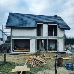 SHARKO SPÓŁKA Z OGRANICZONĄ ODPOWIEDZIALNOŚCIĄ - Surowy stan dwukondygnacyjnego domu z szarej cegły z ciemnym dachem, widoczne schody wewnętrzne, drewniane elementy konstrukcyjne i rusztowania.