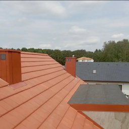 SHARKO SPÓŁKA Z OGRANICZONĄ ODPOWIEDZIALNOŚCIĄ - Czerwona dachówka ceramiczna na skośnym dachu domu jednorodzinnego z kominem w kolorze dachówki. W tle widoczny drugi dom z szarą dachówką.