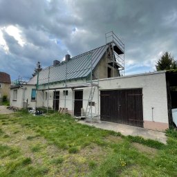 SHARKO SPÓŁKA Z OGRANICZONĄ ODPOWIEDZIALNOŚCIĄ - Dom jednorodzinny w trakcie prac dekarskich, widoczne rusztowania i zabezpieczenia na dachu. Pochmurne niebo w tle.