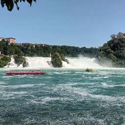 TRAVELSAGE SPÓŁKA Z OGRANICZONĄ ODPOWIEDZIALNOŚCIĄ - Reńskie wodospady w letnim słońcu. Dwa różowe statki wycieczkowe na pierwszym planie, zamek na wzgórzu w tle. Turystyczna atrakcja w Szwajcarii.