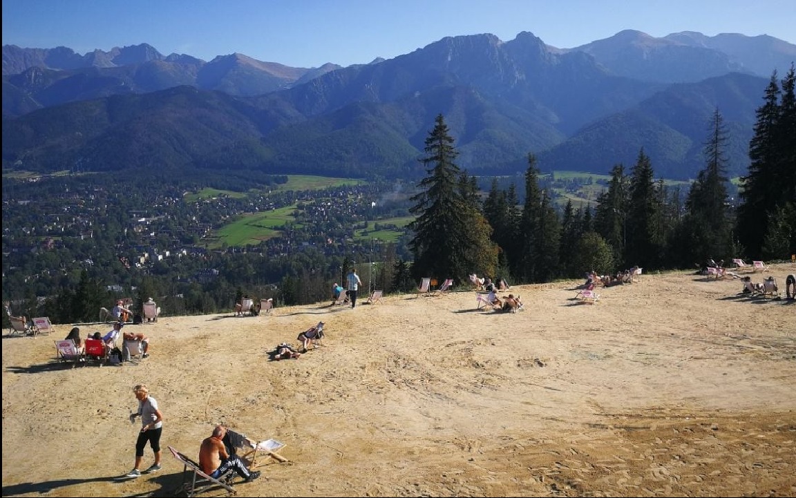 Widok na Zakopane z Gubałówki. Ludzie relaksują się na leżakach, w tle panorama Tatr. Słoneczny dzień, wypoczynek na świeżym powietrzu.