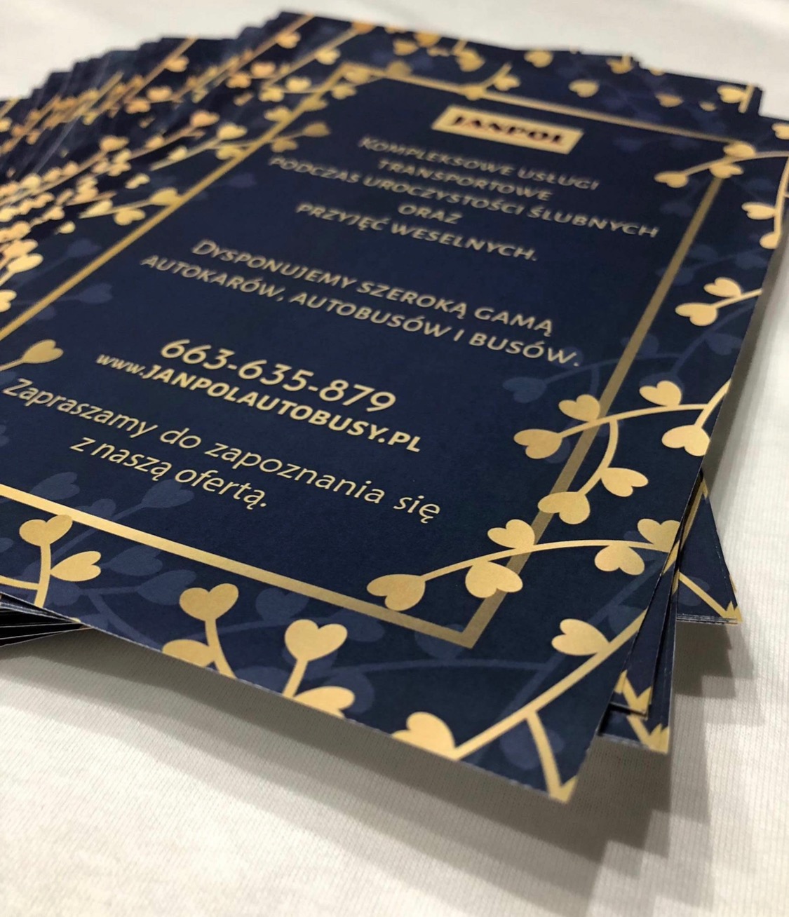 Stos niebieskich wizytówek z dekoracyjnym złotym obramowaniem i informacjami o transporcie okolicznościowym, ułożonych pod kątem na białym podłożu.