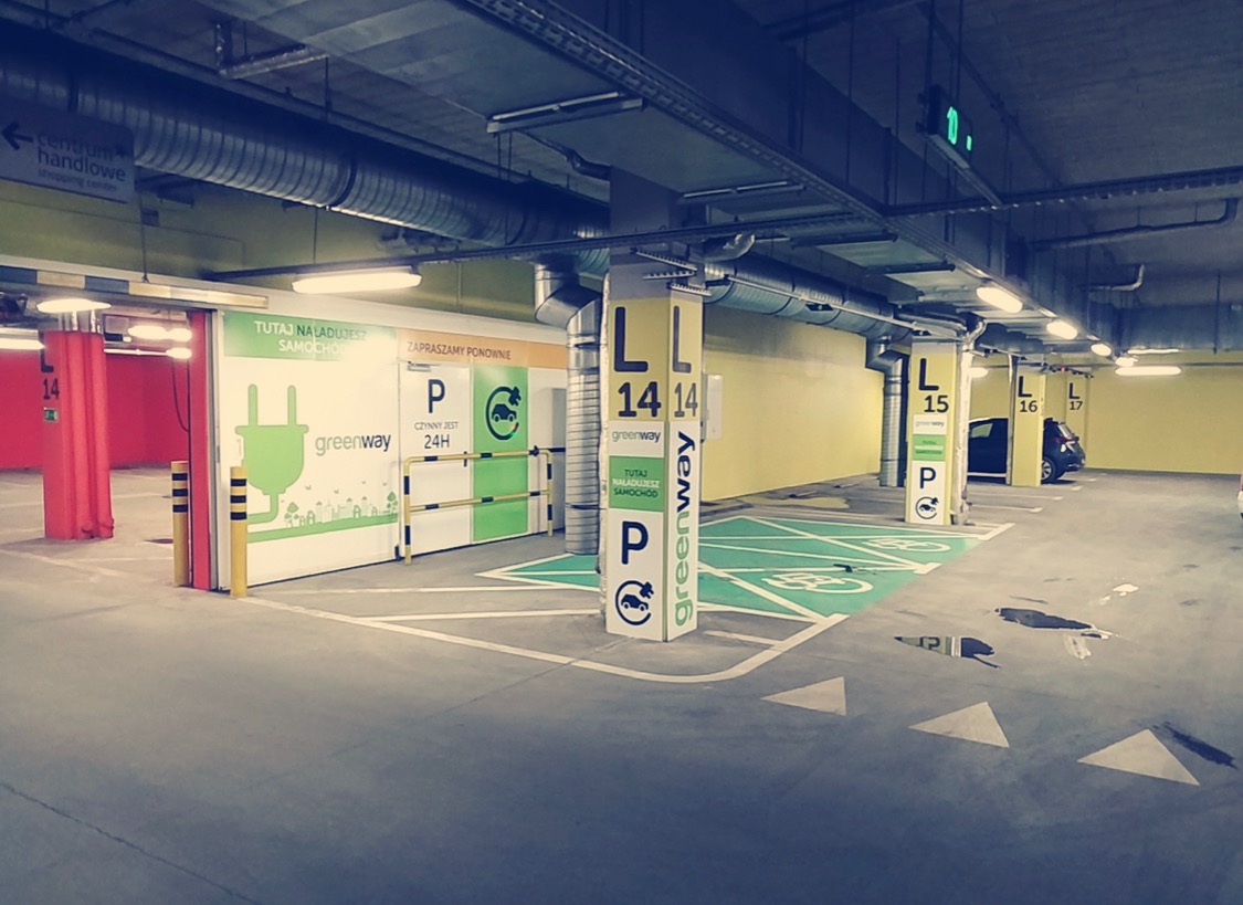 Oznakowane stanowiska do ładowania samochodów elektrycznych w garażu podziemnym, z kolumnami z numeracją miejsc i logo Greenway.
